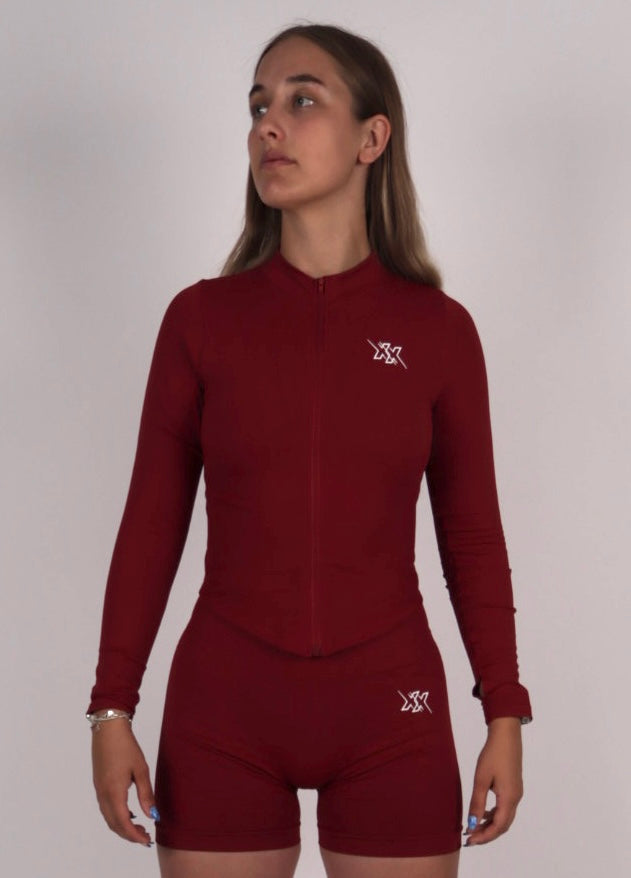Vrouwelijk model draagt de Wine Red Sculpt Vest en Sculpt Legging gymwear uit de Sculpt Collection van Next Extreme Performance, kijkend opzij voor een stijlvolle en sportieve look.